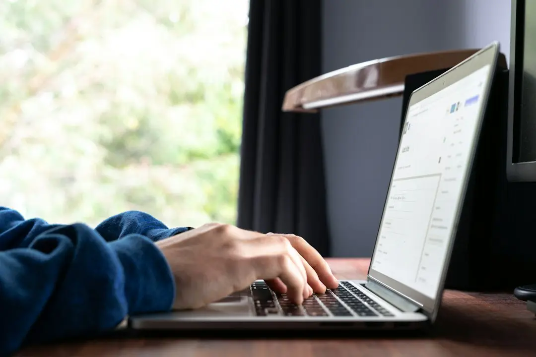 A person typing on a laptop by a window while checking an IPTV provider such as Lux IPTV