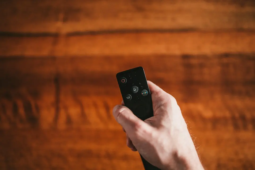 A hand holding a TV remote against a wooden wall, ready to set up Lux IPTV on a smart TV